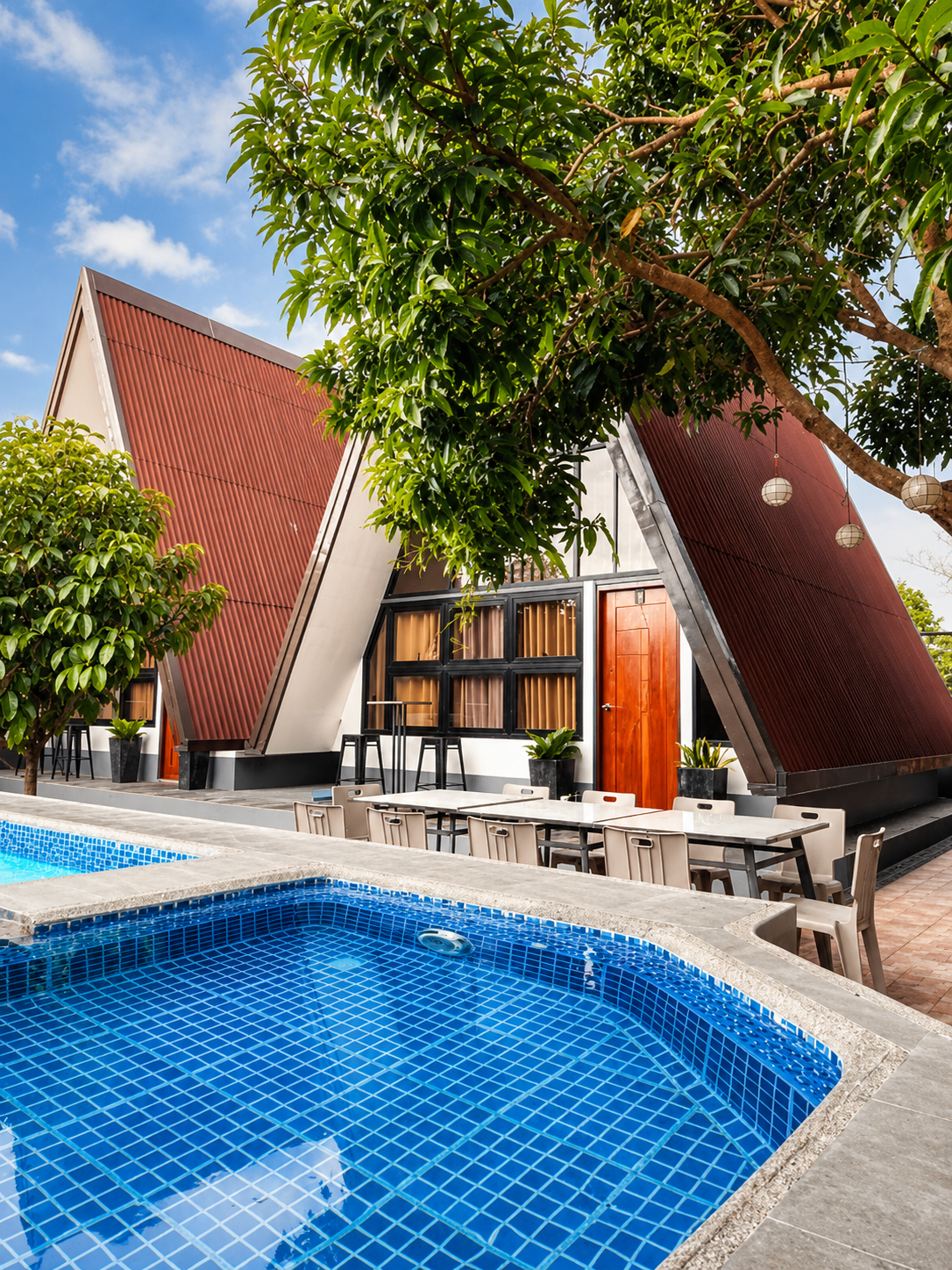 De Grano's Homestay at dusk — lit A-frame villa beside the swimming pool and open-air pavilion